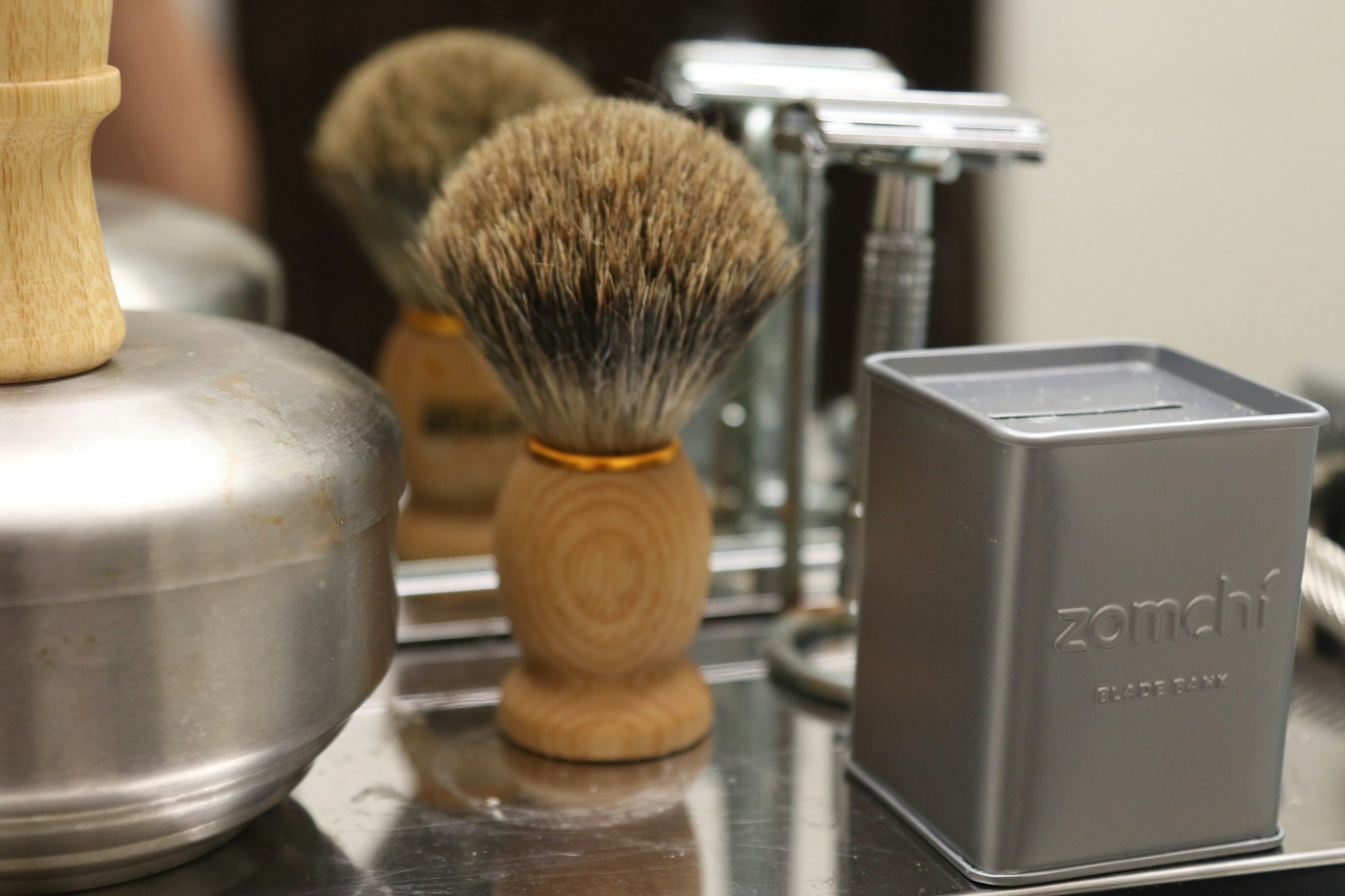A wooden shaving brush beside chrome safety razors