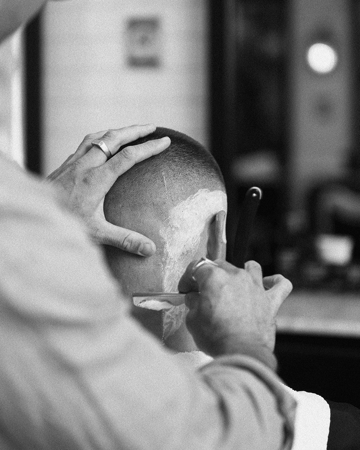 Black-and-white photograph of a barber detailing a haircut with a straight razor